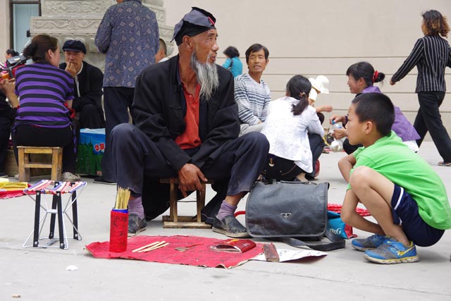 武威雷台（中国）の縁日で筮竹占い師を興味深く眺める子